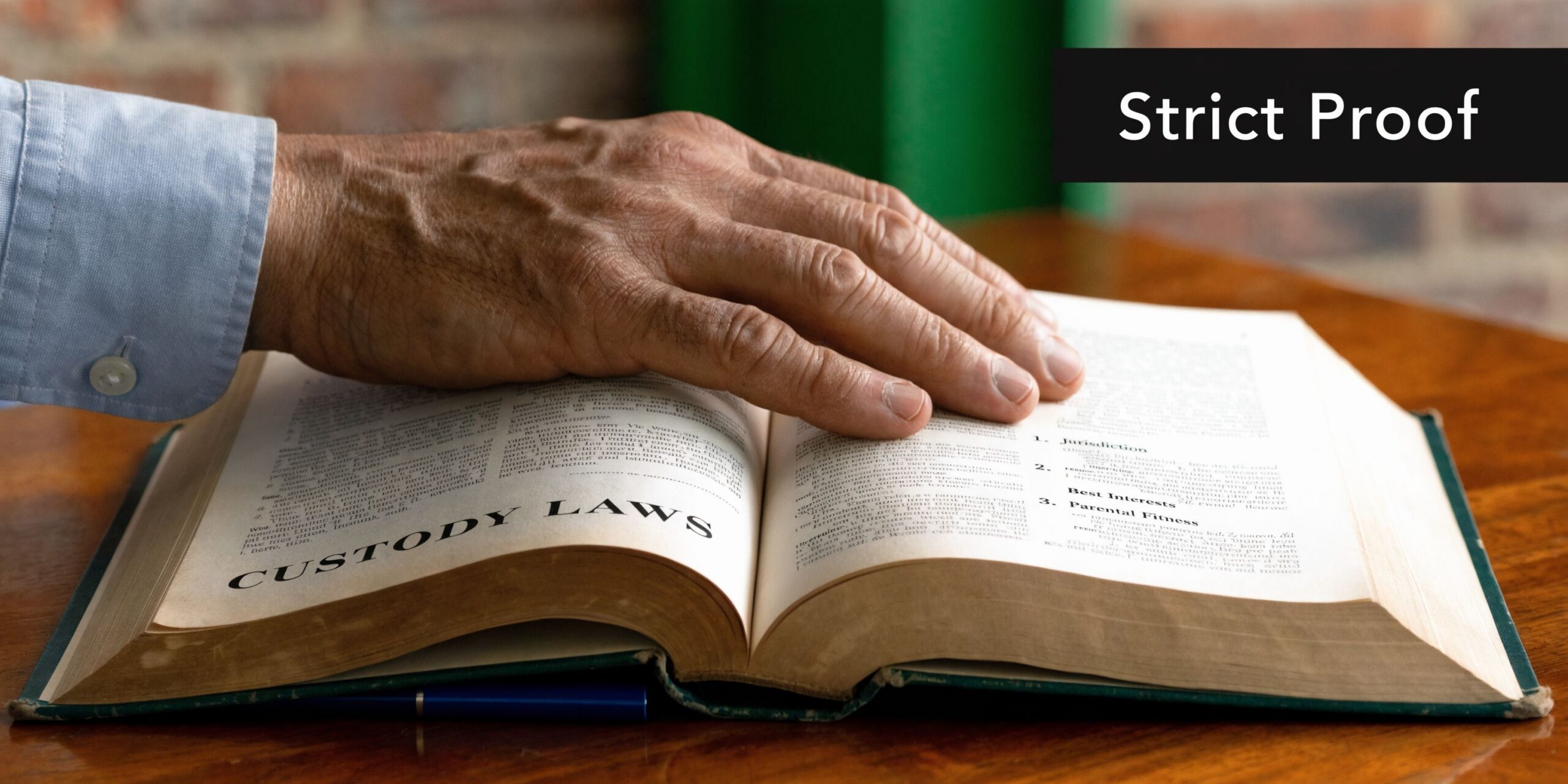 A man's hand resting on an open book titled Custody Laws on a wooden desk.