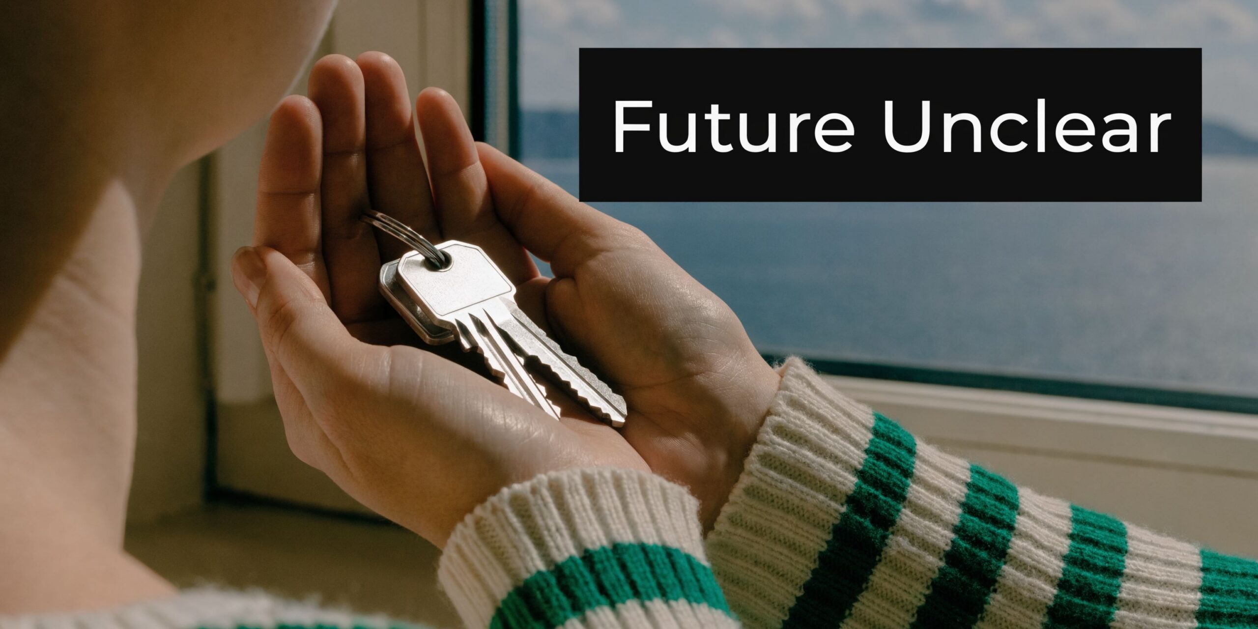 A person holding a set of keys in their cupped hands with a view of the sea.