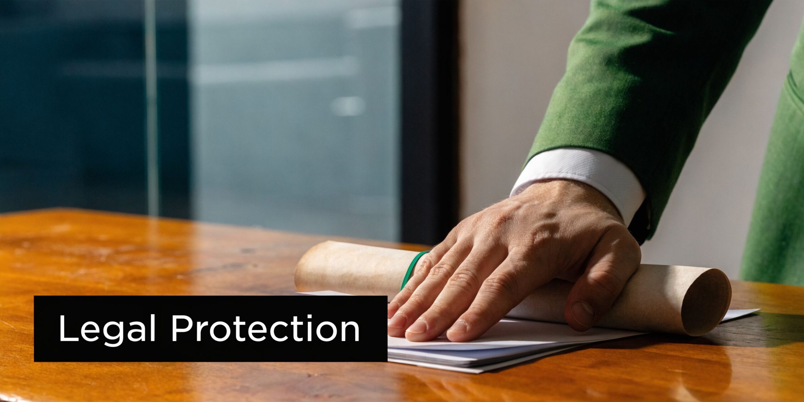 A professional in a green suit hand resting on a rolled legal document on a wooden table.